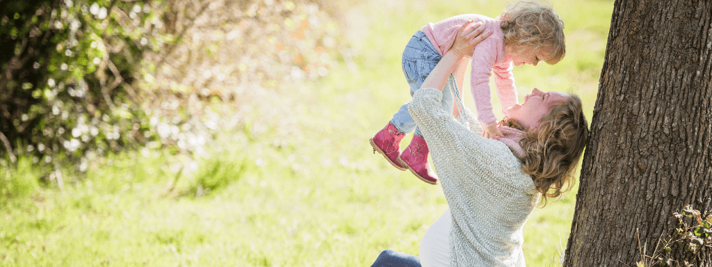 Outdoor baby class: image shows a pregnant woman holding her baby in the air playfully